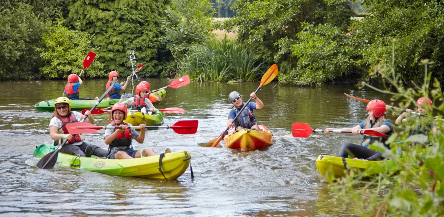 A volunteer paddling alongside laughing campers at Camp Perthes UK