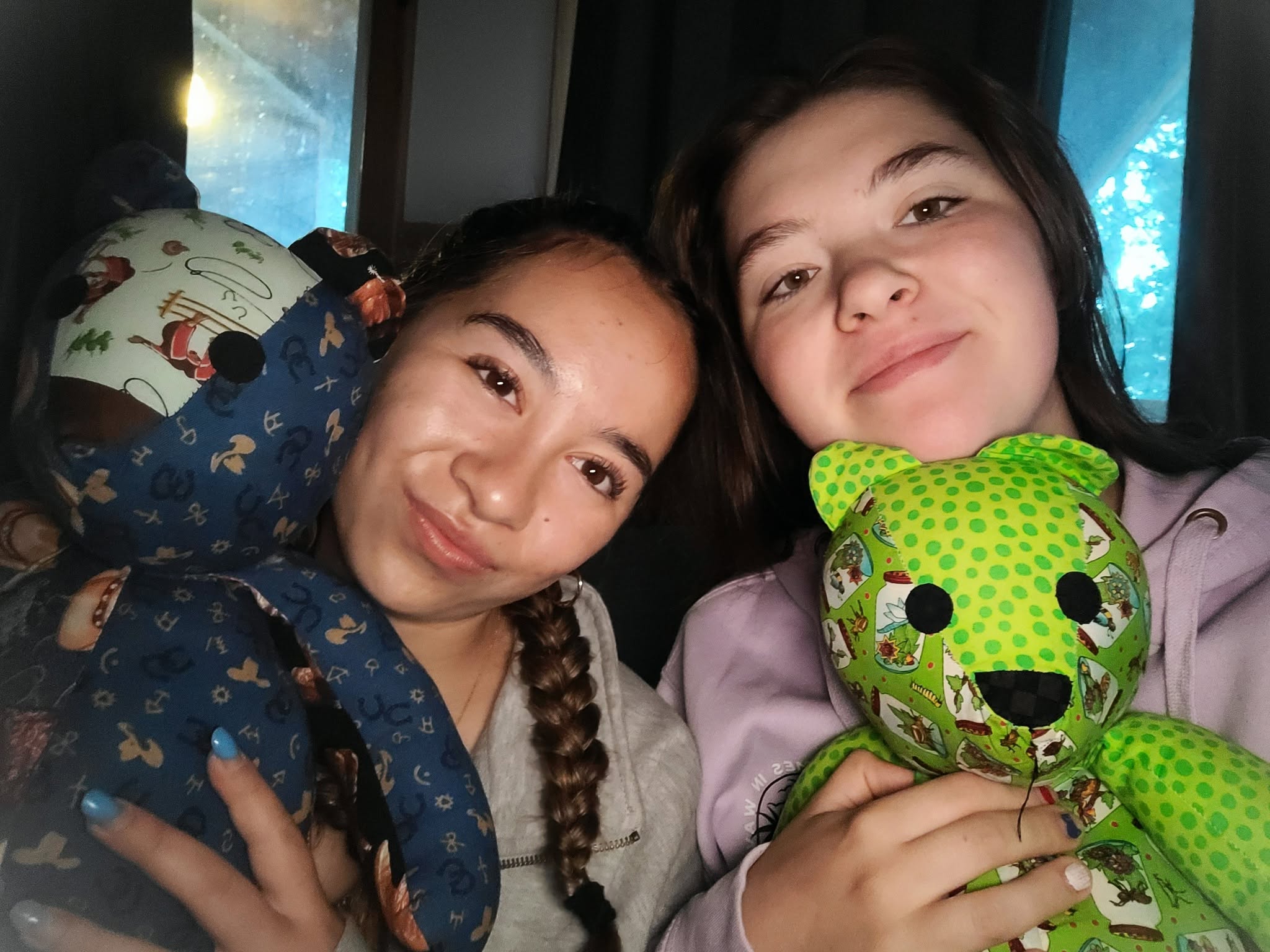 Two teen campers resting cheek to cheek, holding handmade memory bears at Camp Perthes